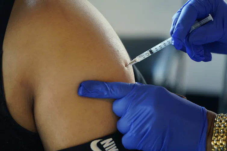 Des mains gantées faisant une injection dans une épaule