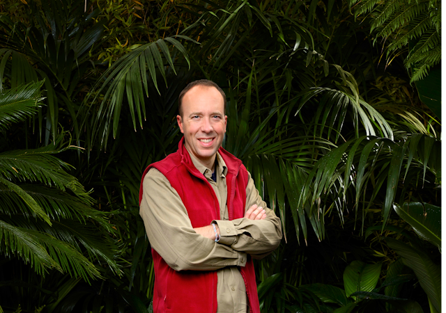 Man in red vest in jungle smiles with arms crossed. 
