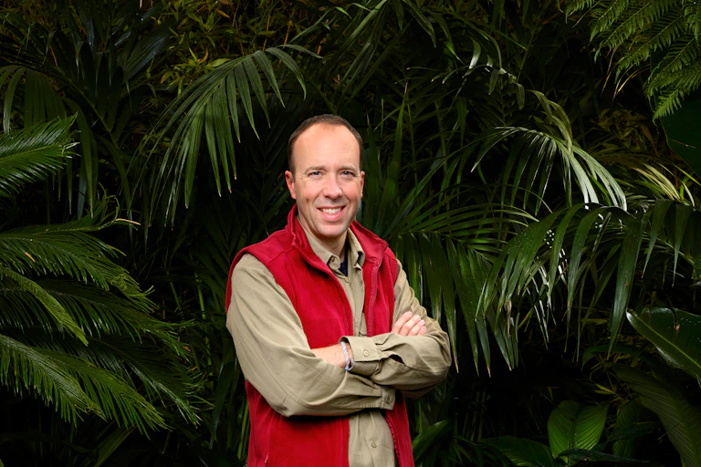 Man in red vest in jungle smiles with arms crossed.