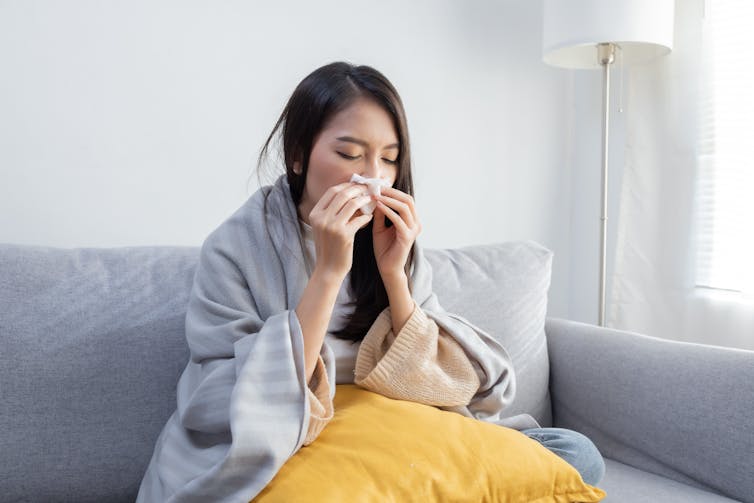 A woman sitting on the couch blowing her nose.