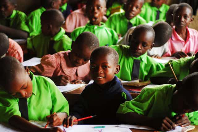 Boys and girls in school uniform writing in books in a classroom.
