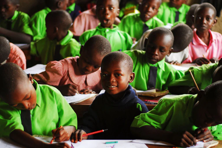 Boys and girls in school uniform writing in books in a classroom.