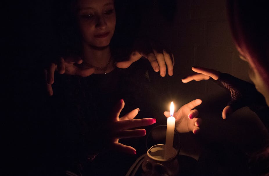 Women practicing witchcraft by burning a candle in a dark room.