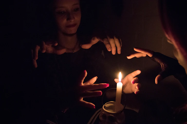 Women practicing witchcraft by burning a candle in a dark room.