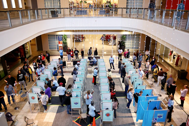 A view from above shows many small cubicles in which people are standing and making selections on screens.