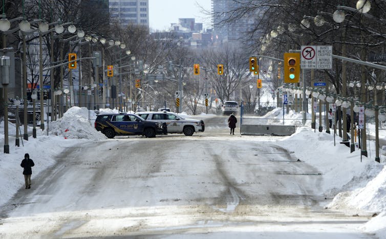 Police seen on a snowy street at a fenced-in area.