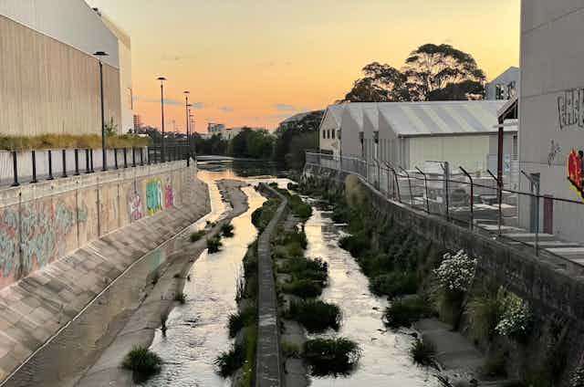 a concrete-lined water course runs between old industrial buildings