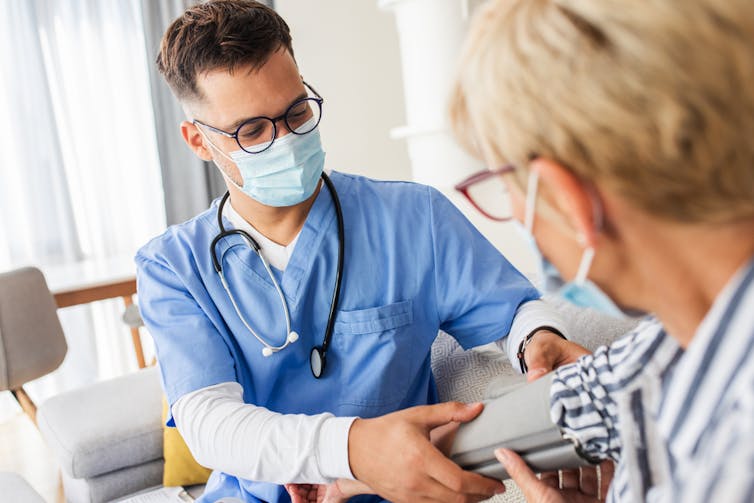 Male nurse wearing mask taking blood pressure of female patient wearing mask