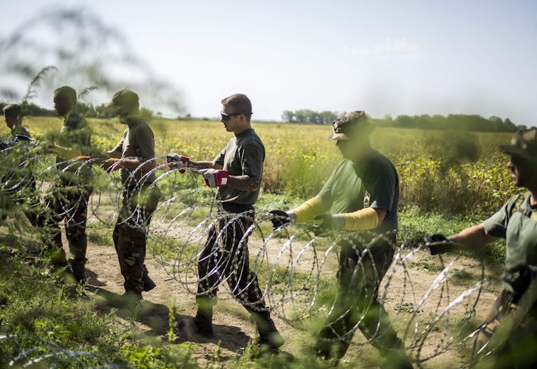 Soldiers setting up rings of razor wire along a rural road