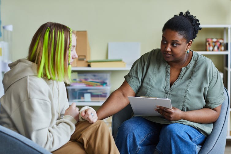 A mental health worker counselling a young woman with green hair