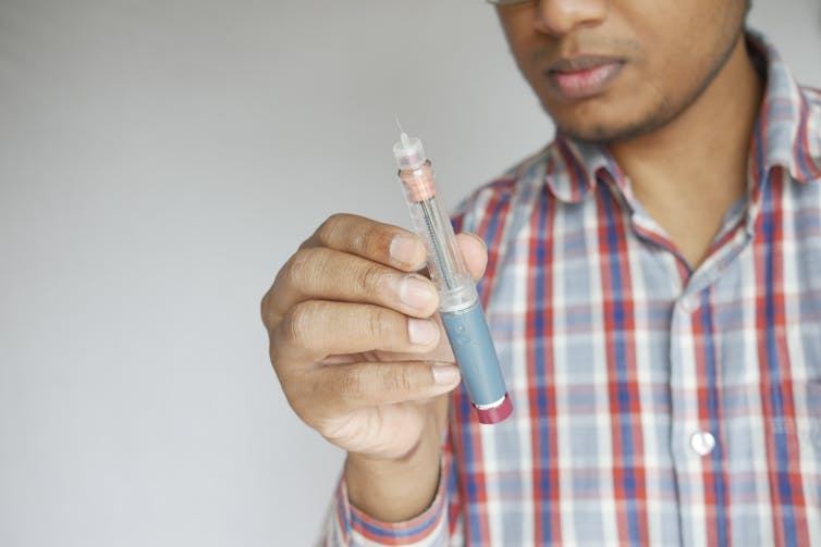 Cropped image of a young man in a plaid shirt holding an insulin pen for Type 2 diabetes