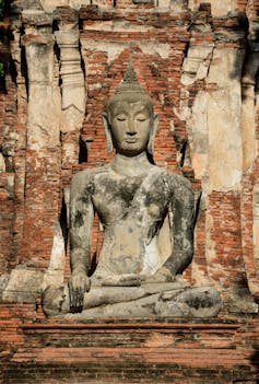 A statue of Buddha against a backdrop of pillars and reddish stones.