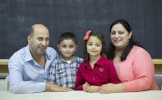 Smiling parents pose for a photo with their two smiling children between them.