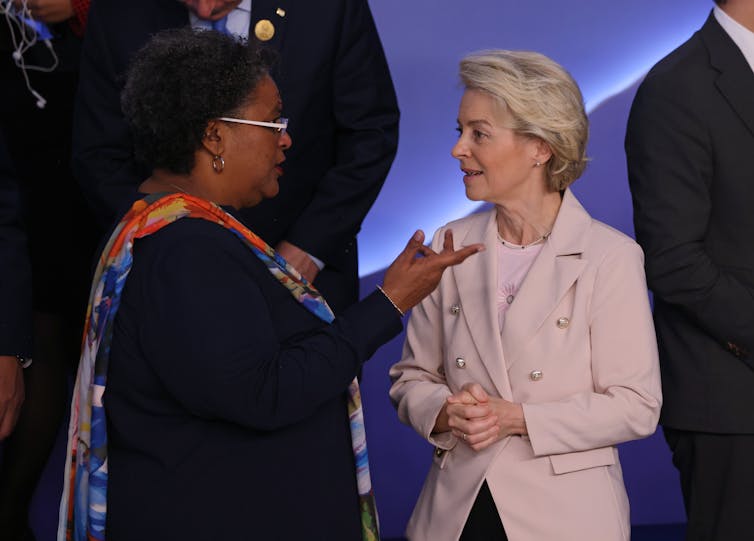 Standing together in a meeting room, Mia Motley speaks and gestures while Ursula von der Leyen listens intently.