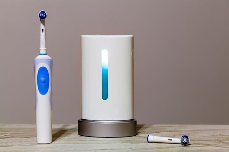 A stock photograph of an electric toothbrush next to a white container with a blue light in the centre