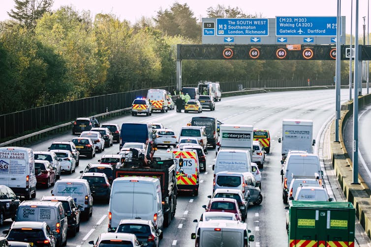 O tráfego parou diante de um pórtico de autoestrada com uma pequena faixa laranja pendurada na lateral.