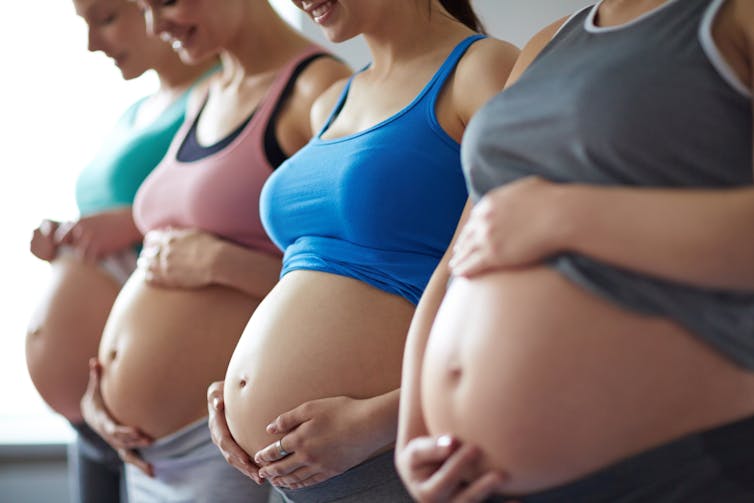 Four pregnant women wearing sports bras and cradling their bellies