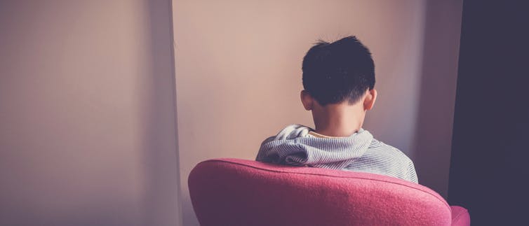 A child sitting on a red chair facing away. The child has dark hair and grey hoodie. Autism and ADHD: the youth justice system is harming neurodivergent children