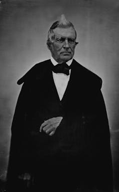 A black-and-white photo of a man in a suit with grey hair.