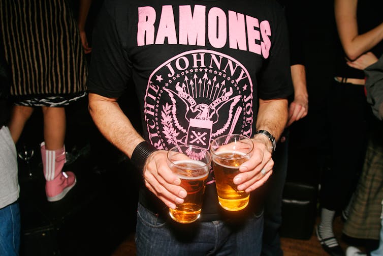 Close up of person holding pints of beer wearing a Ramones t-shirt.