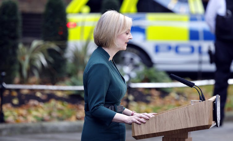 Liz Truss, green dress, lecturn, outside, police car and cordon.