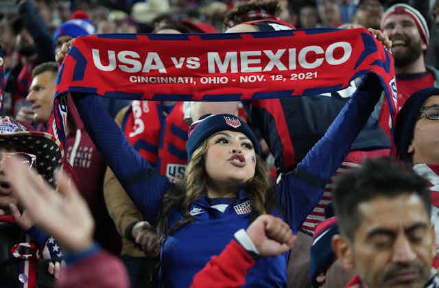 A woman holds up a scarf with 'USA vs Mexico' written on it.