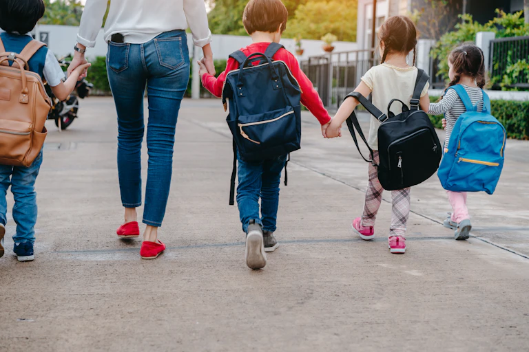 A woman and four small children hold hands in a street setting.