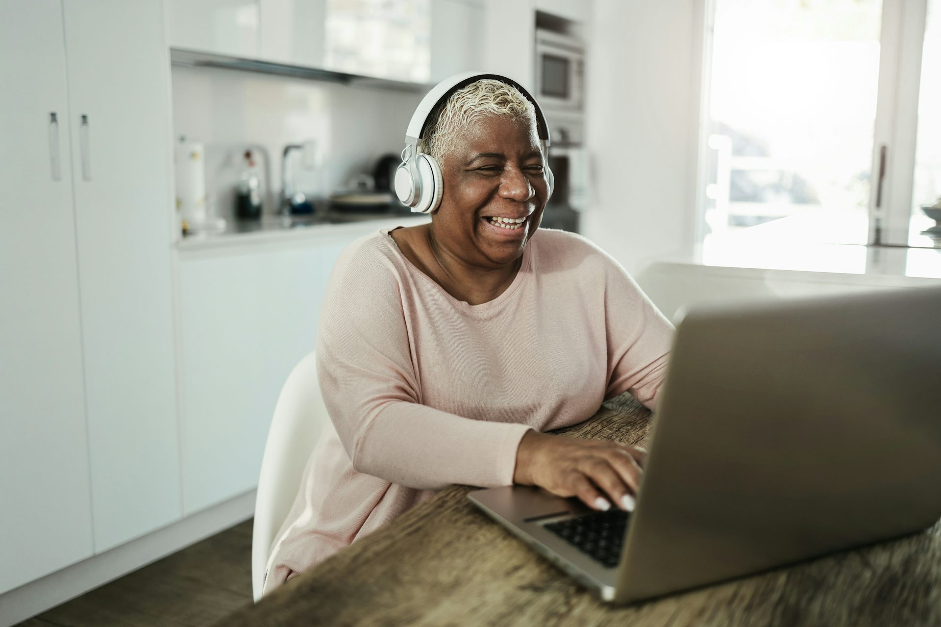 A woman in headphones laughing while looking at computer screen.