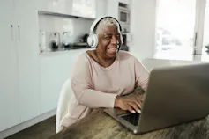 A woman in headphones laughing while looking at computer screen.