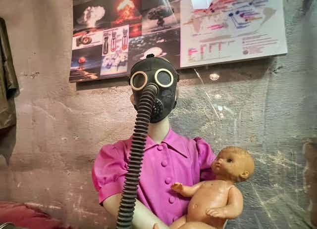 Mannequin in gas mask holding a baby doll