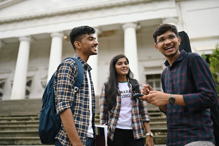 Three students stand in front of the steps of a college building with pillars.