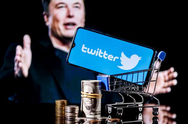 A smartphone displaying the Twitter logo above a pile of cash with an image of Elon Musk in the background.
