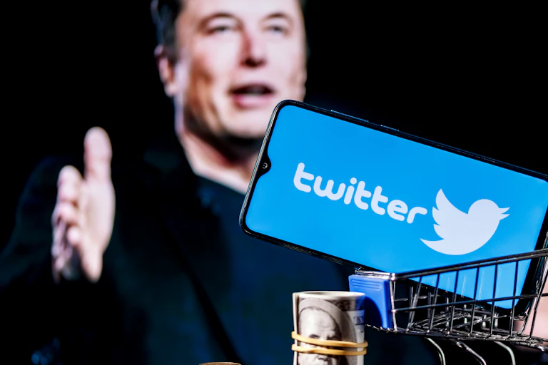 A smartphone displaying the Twitter logo above a pile of cash with an image of Elon Musk in the background.