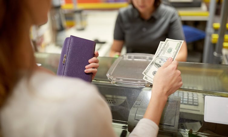 A woman handing a handful of bills to a cashier