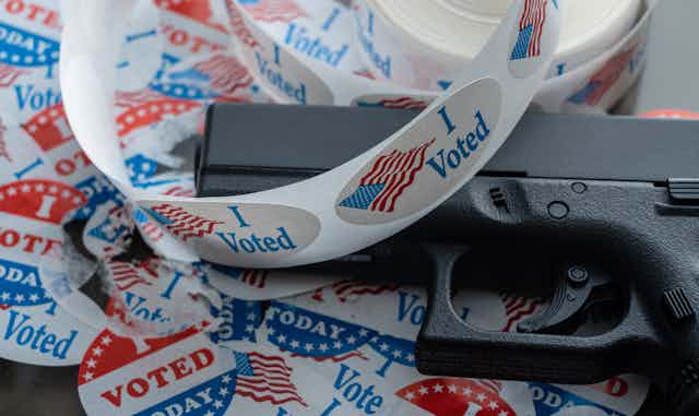 A handgun is seen with 'I voted' stickers around it.