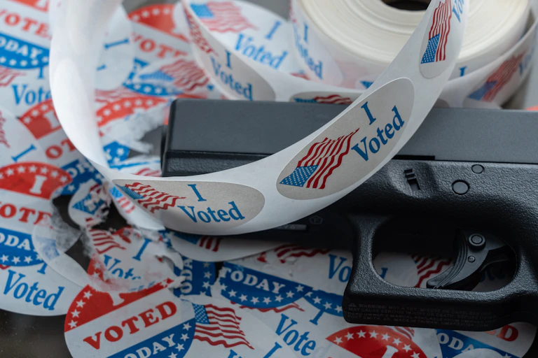 A handgun is seen with 'I voted' stickers around it.
