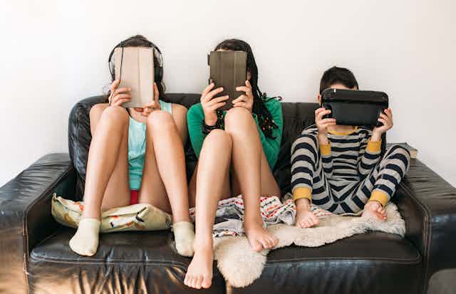 Three children on a couch with digital devices covering their faces
