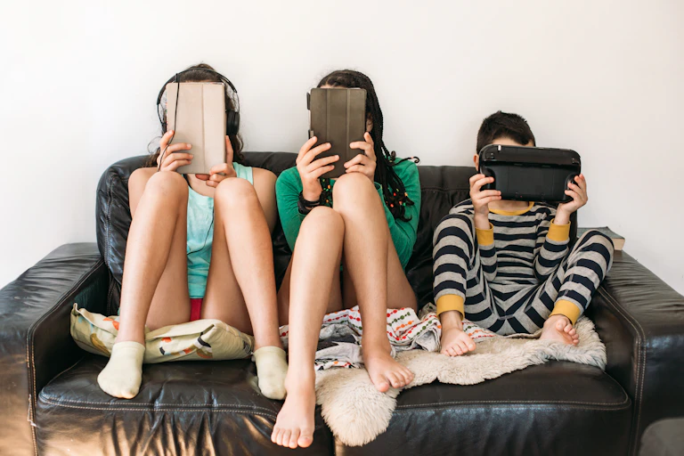 Three children on a couch with digital devices covering their faces