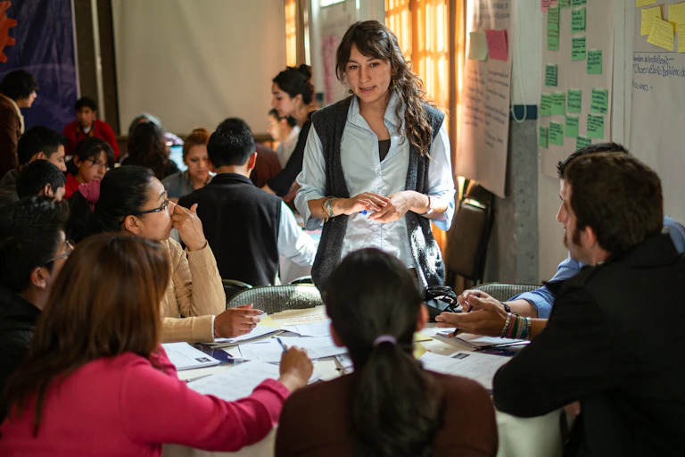 A standing woman speaks to people seated around a table.