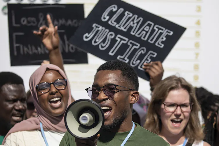 A man holds a megaphone while people chant and hold signs reading 'climate justice' behind him.