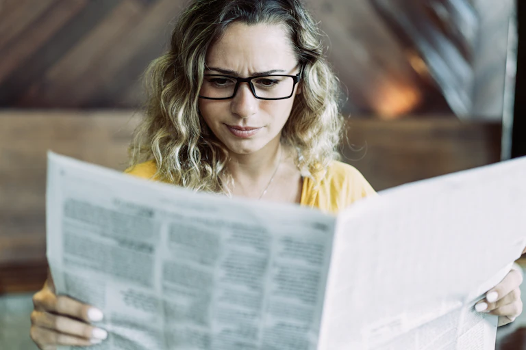 A woman reads a newspaper.