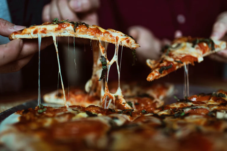 Two people picking up pizza slices from a box