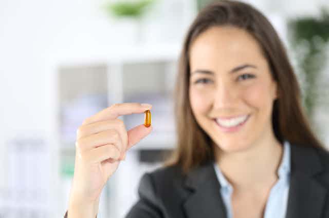 Una mujer sonriente muestra una píldora dorada entre los dedos.