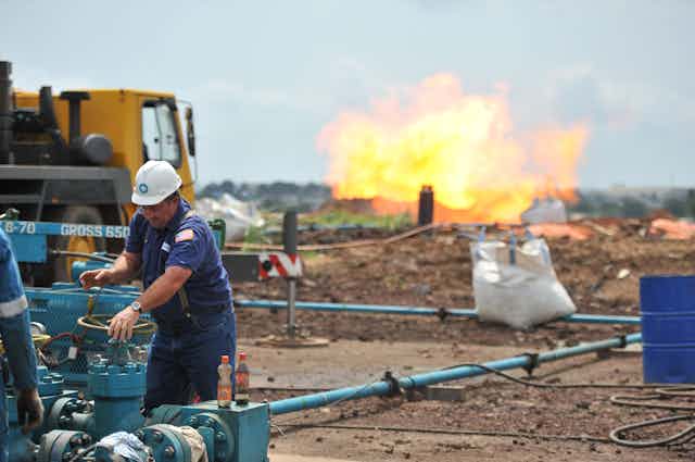 A worker in hard hat turns a valve with a gas flare in the background.