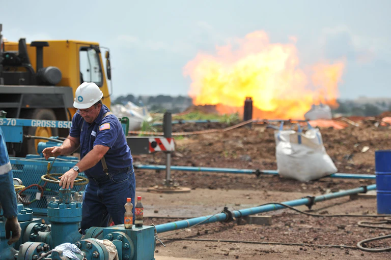 A worker in hard hat turns a valve with a gas flare in the background.