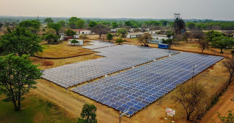 A ground-mounted solar farm surrounded by trees and houses.