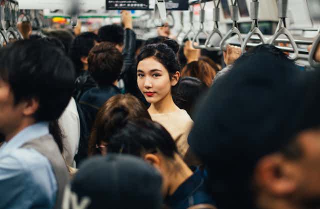 A woman looks at the camera from inside a packed metro carriage