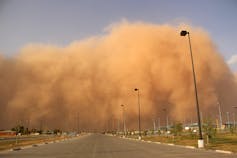 A large cloud of dust moving down a road against a clear blue sky.