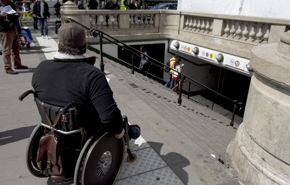 Un homme handicapé en fauteuil roulant distribue des tracts en haut des escaliers d'une station de métro alors qu'il participe à une manifestation à l'appel de l'Association des paralysés de France (APF) pour réclamer plus d'accessibilité dans leur vie quotidienne, le 13 mai 2014 à Paris.