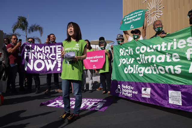 Un activista está de pie con sus colegas sosteniendo carteles que dicen "Financiación climática ya" y "Países ricos: paguen sus obligaciones de financiación climática ya".